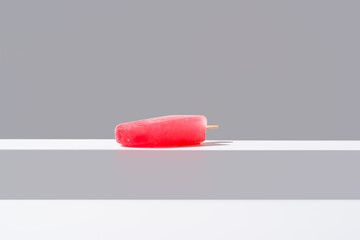 Polo de hielo rojo. Palo de helado sabor a fresa sobre fondo gris y blanco	