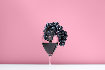 Copa de vino tinto con uvas negras sobre fondo rosa