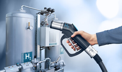 Hand with hydrogen fueling nozzle on a background of H2 factory. Hydrogen production from renewable energy sources concept