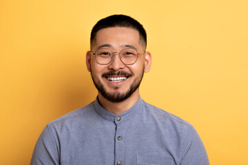 Fototapeta premium Portrait of happy handsome asian man posing on yellow studio background