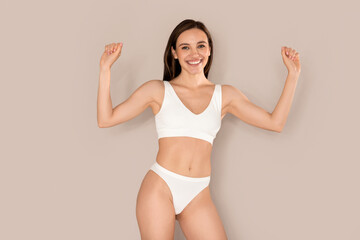 Excited happy young woman in underwear celebrating success on beige