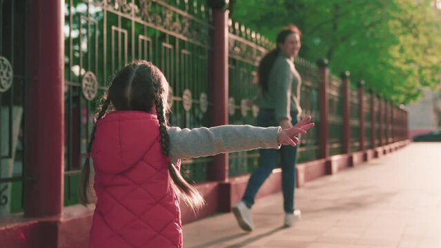 Child, daughter runs to mom and hugs her in park on street in spring. Happy family. Carefree childhood, joyful run of baby to mother. Small child cheerfully plays in summer on street with parent.