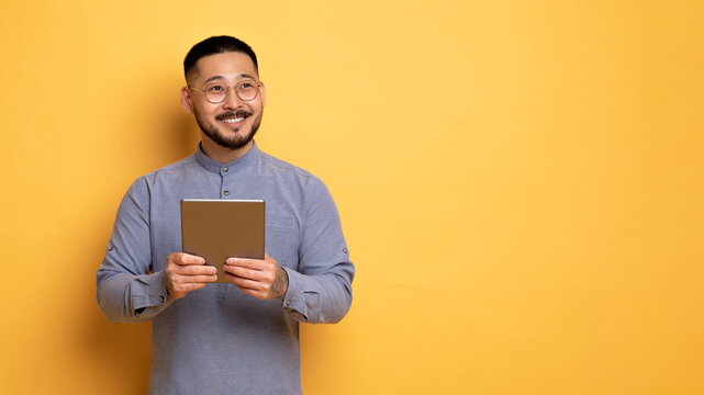 Young Smiling Asian Man Holding Digital Tablet And Looking Away