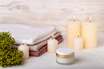 Obraz na płótnie Canvas Burning candles and face cream, towels and juniper branch on light background. Concept of calmness, comfort, spa treatments. Selective focus