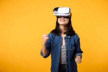 Young asian woman happy success wearing virtual reality headset game entertainment isolated on yellow background. Winner of cyber future video game concept.