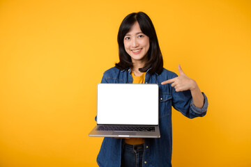 Fototapeta na wymiar portrait young happy woman wearing yellow t-shirt and denim shirt holding laptop and point finger to screen isolated on yellow studio background. business technology application communication concept.