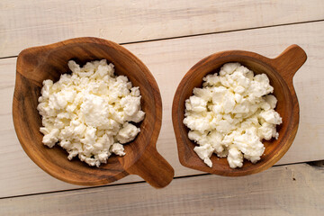 Fresh cottage cheese in two wooden cups on a wooden table, macro, top view.