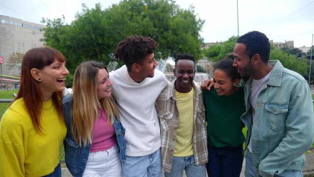 Young group of happy diverse people hugging each other laughing together outdoor. Millennial united friends enjoying time social gathering in city street. Youth community concept.