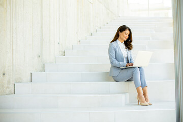 Young business woman sitting on the stairs on office hallway and working on laptop