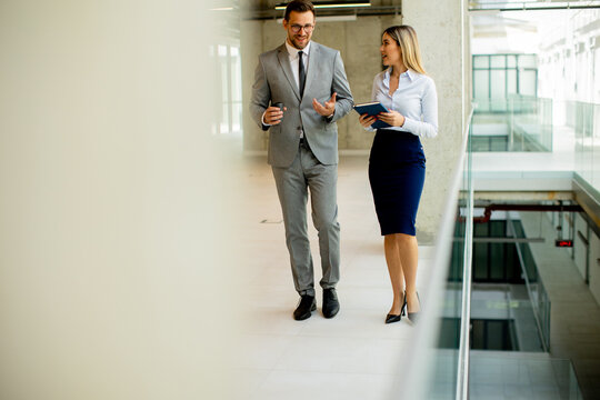 Young Coworkers Walking And Talking Along Corridor In Modern Office