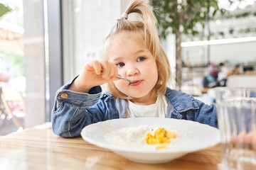 Little kid having breakfast at cafe. Adorable girl drinking still water, eating rice porridge with mango. enjoying breakfast.