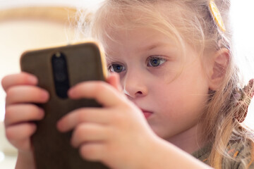 A little girl is looking intently at her phone. Children and modern technology. Phone dependency