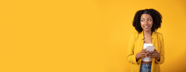 New application advertisement concept. Happy black woman using mobile phone, yellow background, panorama, copy space