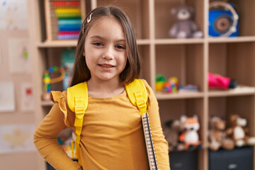 Adorable hispanic girl student smiling confident holding notebook at kindergarten