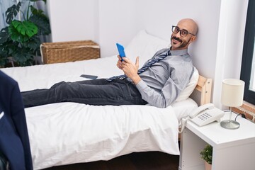 Young hispanic man business worker using touchpad lying on bed at hotel room