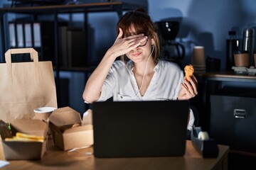 Young beautiful woman working using computer laptop and eating delivery food covering eyes with hand, looking serious and sad. sightless, hiding and rejection concept