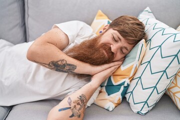 Young redhead man lying on sofa sleeping at home