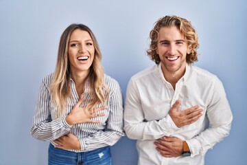 Young couple standing over blue background smiling and laughing hard out loud because funny crazy joke with hands on body.