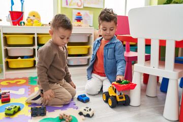 Adorable boys playing with cars toy and tractor sitting on floor at kindergarten