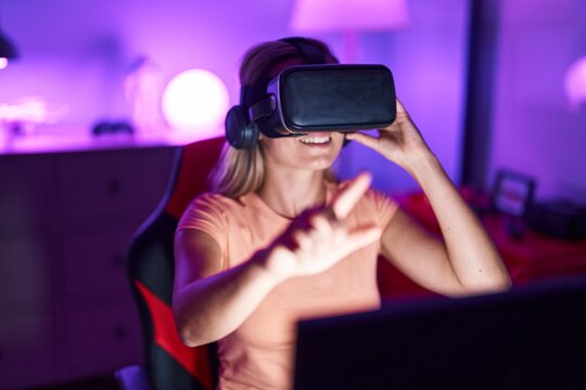 Young blonde woman streamer playing video game using virtual reality glasses at gaming room