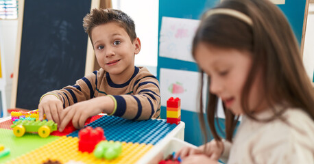 Adorable boy and girl playing with construction blocks sitting on table at kindergarten