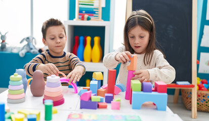 Adorable boy and girl playing with construction blocks sitting on table at kindergarten