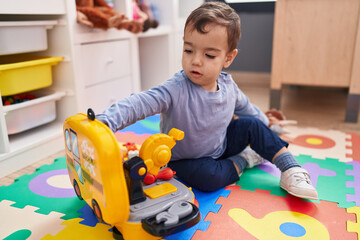 Adorable hispanic boy playing with tools toy sitting on floor at kindergarten