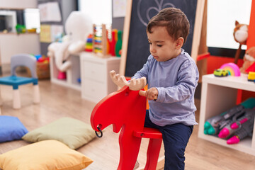 Adorable hispanic boy playing with reindeer rocking at kindergarten