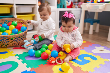Fototapeta na wymiar Adorable boy and girl playing with balls sitting on floor at kindergarten