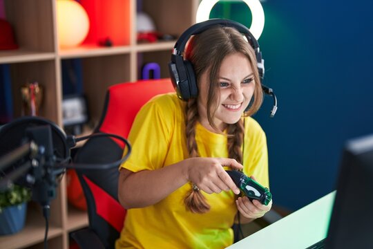 Young blonde woman streamer playing video game using joystick at gaming room