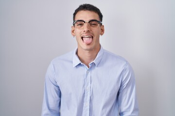 Handsome hispanic man wearing business clothes and glasses sticking tongue out happy with funny expression. emotion concept.