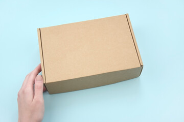 Female hands holding brown ecological package box made of natural corrugated cardboard.