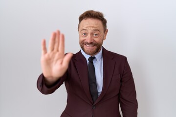 Middle age business man with beard wearing suit and tie waiving saying hello happy and smiling, friendly welcome gesture