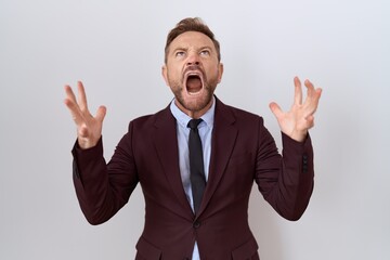 Middle age business man with beard wearing suit and tie crazy and mad shouting and yelling with aggressive expression and arms raised. frustration concept.