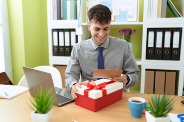 Young hispanic man business worker unpacking gift holding letter at office