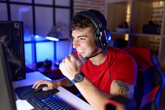 Young hispanic man streamer playing video game with winner expression at gaming room