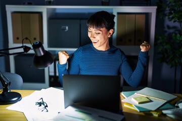 Young beautiful woman working at the office at night very happy and excited doing winner gesture with arms raised, smiling and screaming for success. celebration concept.