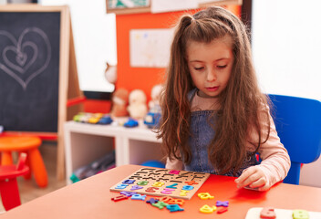 Fototapeta premium Adorable hispanic girl playing with maths puzzle game sitting on table at kindergarten