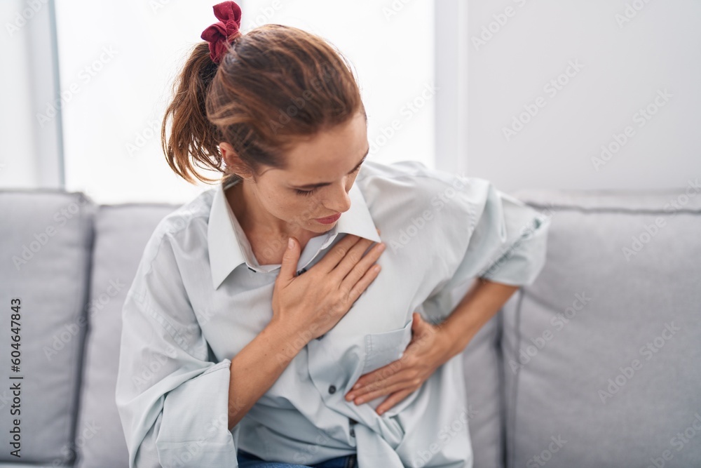 Sticker young woman examining breast sitting on sofa at home