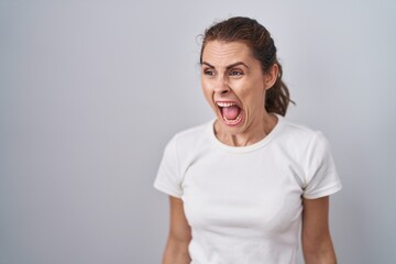 Obraz premium Beautiful brunette woman standing over isolated background angry and mad screaming frustrated and furious, shouting with anger. rage and aggressive concept.