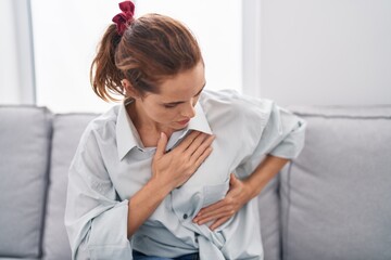 Young woman examining breast sitting on sofa at home