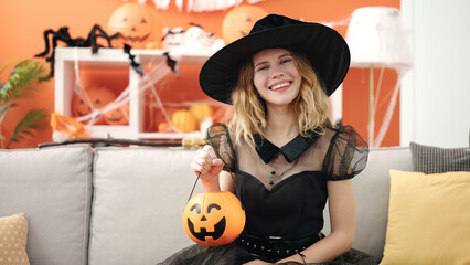 Young blonde woman wearing halloween costume holding pumpkin basket at home