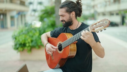 Young hispanic man musician playing classical guitar at park