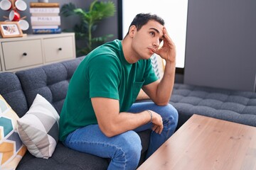 Young hispanic man stressed sitting on sofa at home