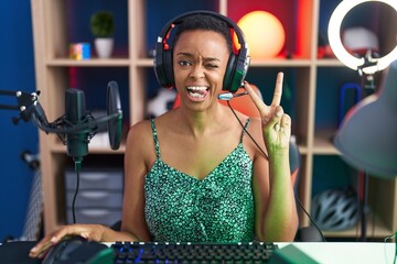 African american woman playing video games smiling with happy face winking at the camera doing...