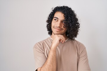 Fototapeta na wymiar Hispanic man with curly hair standing over white background with hand on chin thinking about question, pensive expression. smiling with thoughtful face. doubt concept.