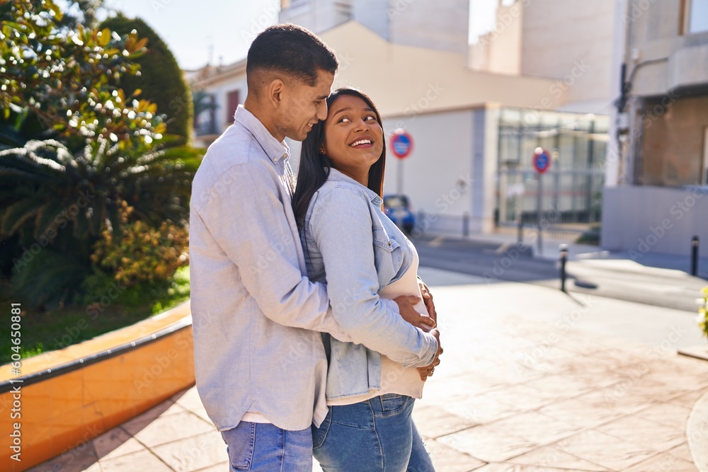 Sticker young latin couple expecting baby hugging each other standing at park