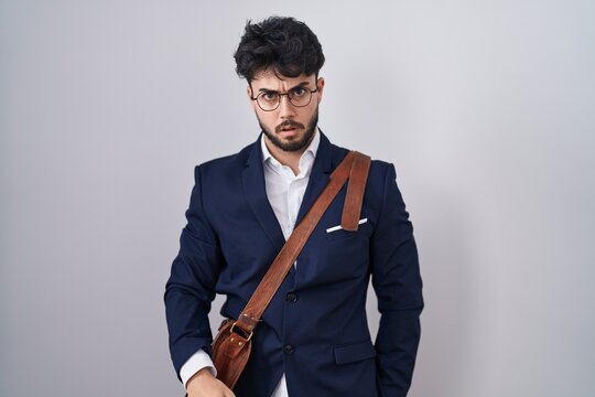 Hispanic man with beard wearing business clothes in shock face, looking skeptical and sarcastic, surprised with open mouth