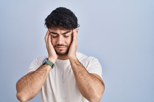 Hispanic man with beard standing over white background with hand on head, headache because stress. suffering migraine.