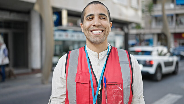 Young hispanic man volunteer smiling wearing vest at street